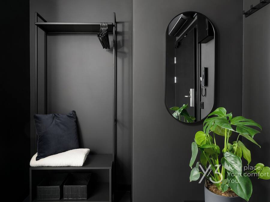 A modern bathroom with a dark color scheme, a built-in bench, a round mirror, and a potted plant.