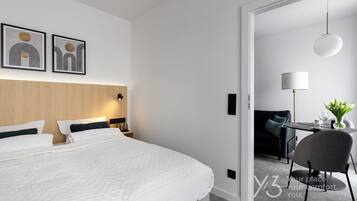 Una habitación de hotel moderna con una cama grande, un cabecero de madera, un escritorio con una silla y una mesa de comedor con un florero.