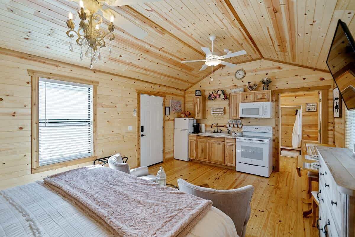A cozy cabin-style room with a bed, a dining table, a kitchen area with appliances, and a ceiling fan.