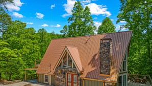 A two-story cabin with a stone chimney, a wooden deck, and a stone foundation. - Selah (Gatlinburg)