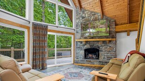 A cozy living room with a stone fireplace, leather sofas, and a large window overlooking a deck. - Selah (Gatlinburg)