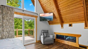 A bedroom with a large bed, a gray recliner, a fireplace, and a sliding glass door to a balcony. - Selah (Gatlinburg)