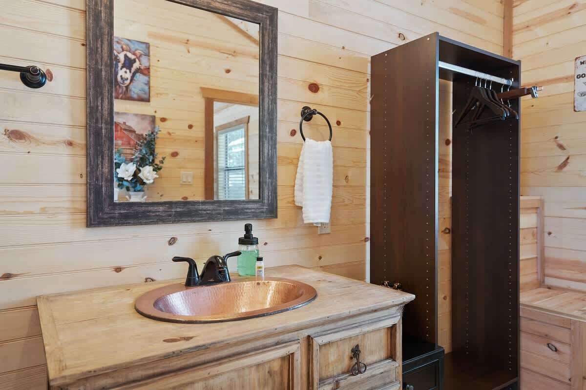A wooden cabin bathroom with a copper sink, a mirror, a towel rack, and a wooden door.