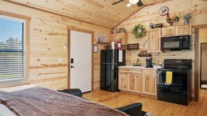A cozy cabin-style room with a wooden interior, a bed with a brown blanket, a ceiling fan, a black refrigerator, a microwave, and a stove. - Gorgeous Cabin on Main-steps to Pacific War Museum (Fredericksburg)