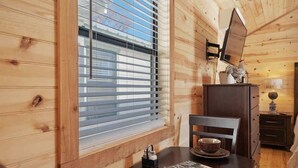 A wooden interior with a dining table, chairs, a window with blinds, a dresser, and a wall-mounted TV. - Gorgeous Cabin on Main-steps to Pacific War Museum (Fredericksburg)