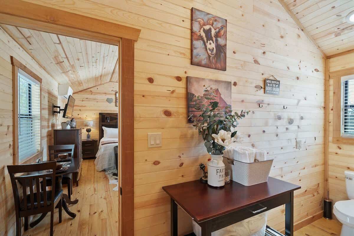 Interior de una cabaña de madera con comedor, cama y baño.