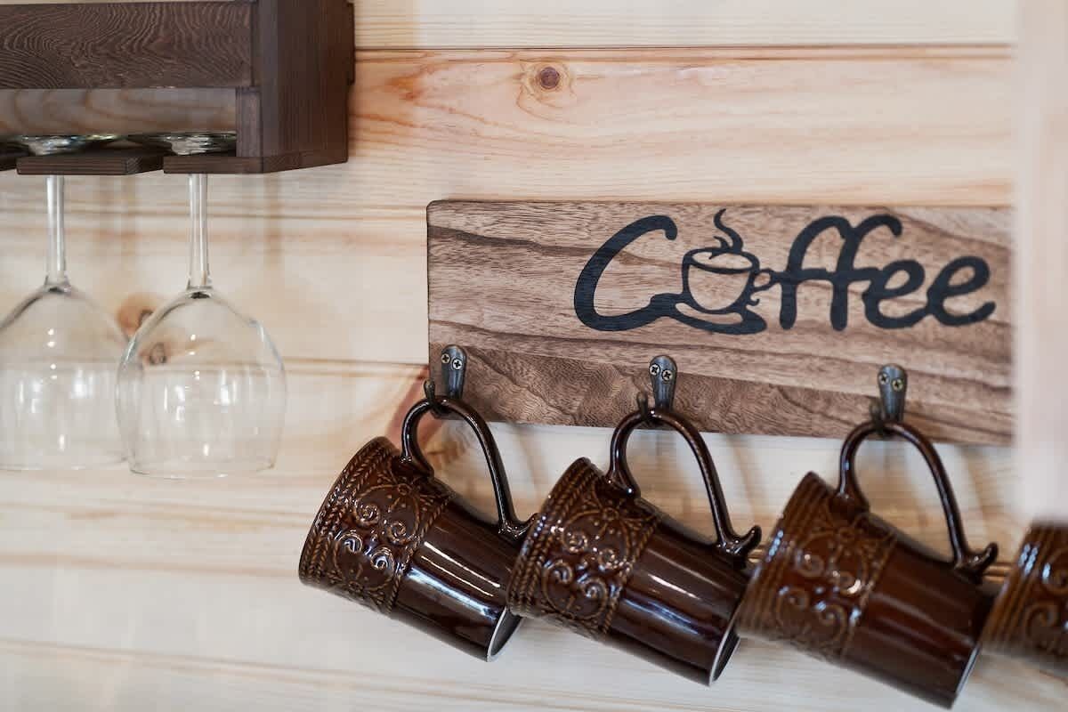 Pared de madera con un letrero que dice “Coffee” y un perchero con varias tazas marrones.