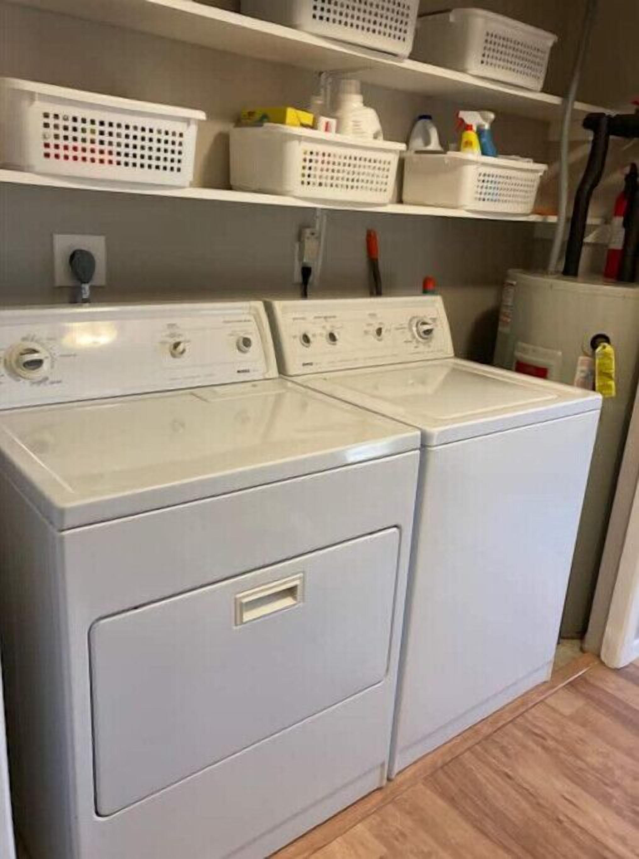 A front-loading washer and dryer unit with a control panel, a white door, and a shelf above holding laundry baskets and cleaning supplies.