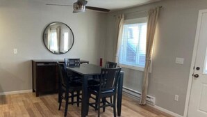 A dining area with a table and chairs, a small cabinet, a ceiling fan, a window with curtains, and a door. - Riverfront Twin Home
 (La Crosse)