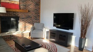 A modern living room with a brick wall, a flat-screen TV, a grey sofa, a coffee table, and a fireplace. - Riverfront Twin Home
 (La Crosse)