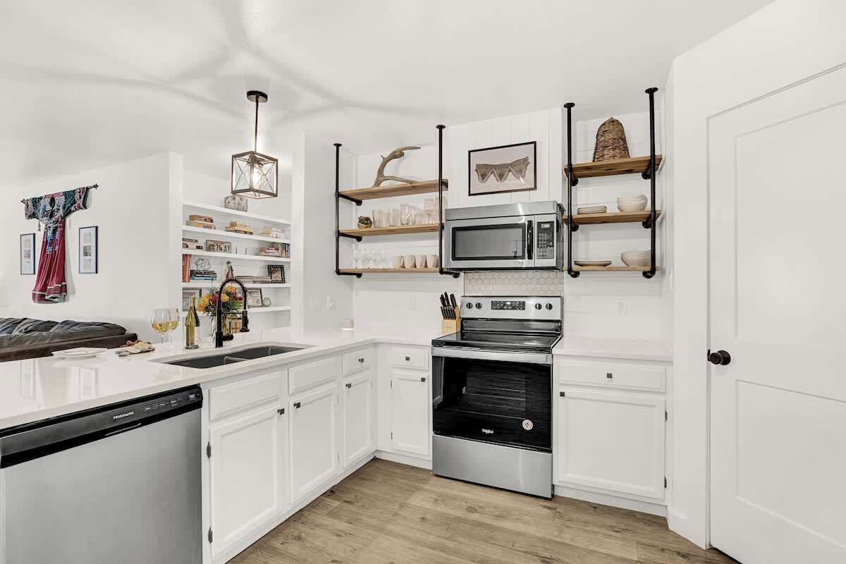 Eine moderne Küche mit weißen Schränken, einer eingebauten Mikrowelle, einem Edelstahlbackofen und Holzregalen.