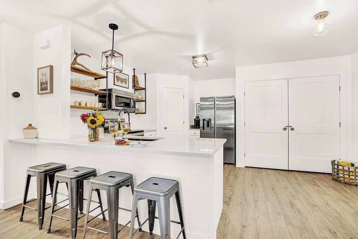 A modern kitchen with a central island, bar stools, stainless steel appliances, and white cabinetry.
