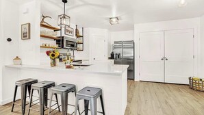 A modern kitchen with a central island, bar stools, stainless steel appliances, and white cabinetry. - Wanderlust #1 Hot Tub Shared Outdoor Space (Fredericksburg)