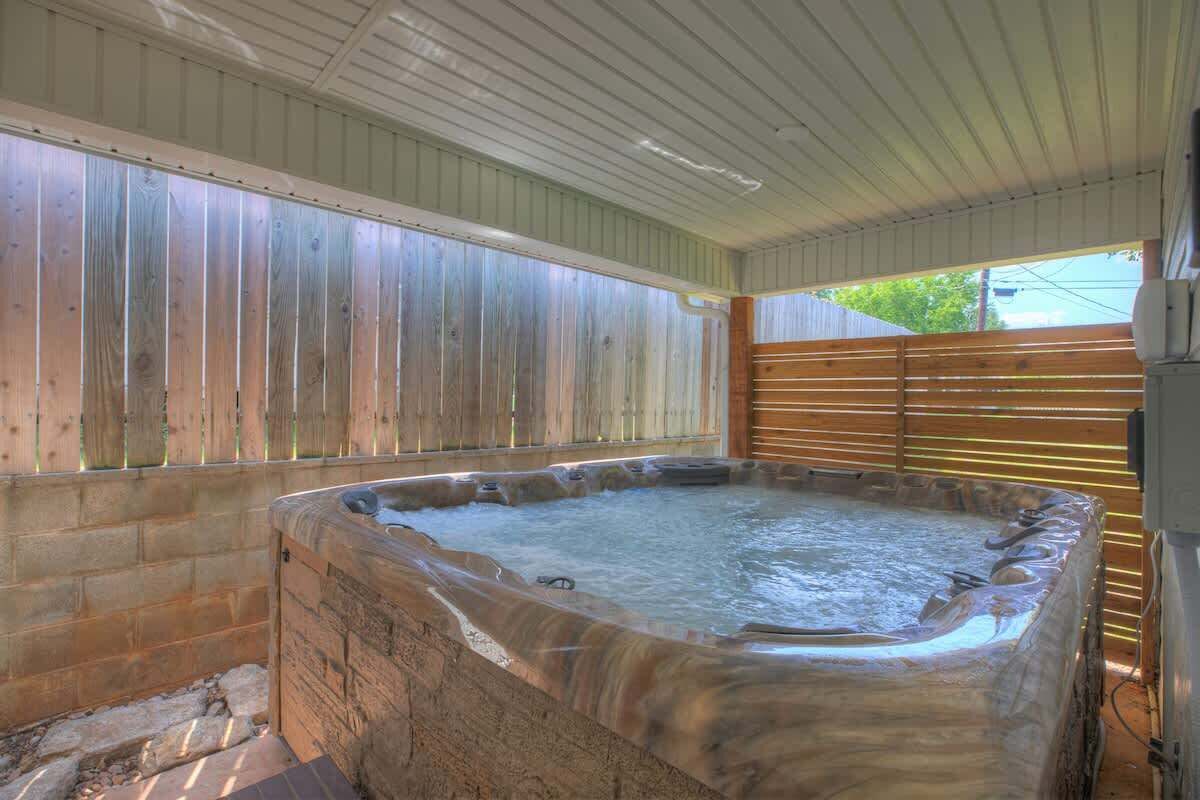 A hot tub under a covered area with wooden walls and a wooden fence.