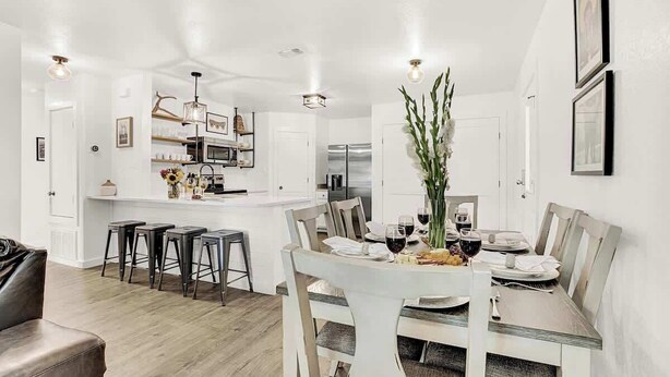 A modern kitchen with white cabinetry, a central island, bar stools, and a dining table set for six. - Wanderlust #1 Hot Tub Shared Outdoor Space (Fredericksburg)