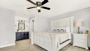 A bedroom with a white bed, a nightstand, a lamp, and a ceiling fan. - Wanderlust #1 Hot Tub Shared Outdoor Space (Fredericksburg)