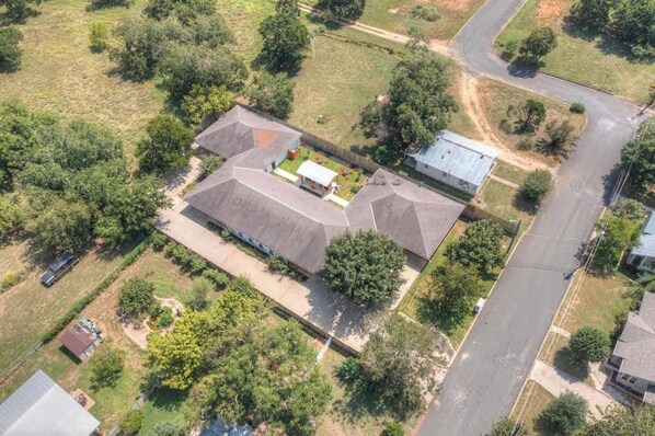 Vue aérienne d’un quartier résidentiel avec une grande maison dotée d’un vaste jardin, d’une allée et d’une route à proximité.