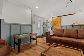 Een kamer met een pooltafel, een bruine leren bank, een houten salontafel en een deur met een houten paneel.
