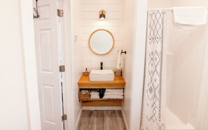 Une petite salle de bain avec un meuble-lavabo en bois, un miroir rond, un porte-serviettes et un rideau de douche à motifs géométriques.