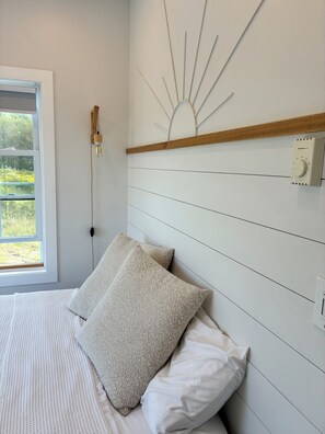 Une chambre à coucher avec un lit, un luminaire fixé au mur et un thermostat.