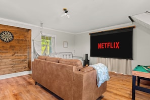 Un salon comprenant un canapé, un jeu de fléchettes, une cheminée et un grand écran affichant le logo « NETFLIX ».