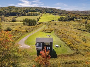 Une maison dotée d’une terrasse, entourée d’un paysage rural, avec un chemin de terre menant à la maison.