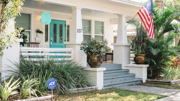 Uma casa branca com uma porta azul-turquesa, uma grande bandeira americana e um letreiro indicando 5% de desconto.