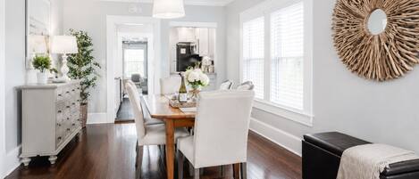 A dining area with a wooden table, white chairs, a black bench, and a decorative wall piece.