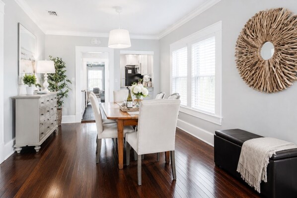 A dining area with a wooden table, white chairs, a black bench, and a decorative wall piece.