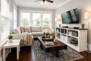 A living room with a sofa, coffee table, TV, bookshelf, and a window with blinds.