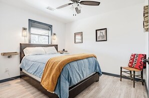 Un dormitorio con una cama, una silla, un ventilador de techo y una ventana.