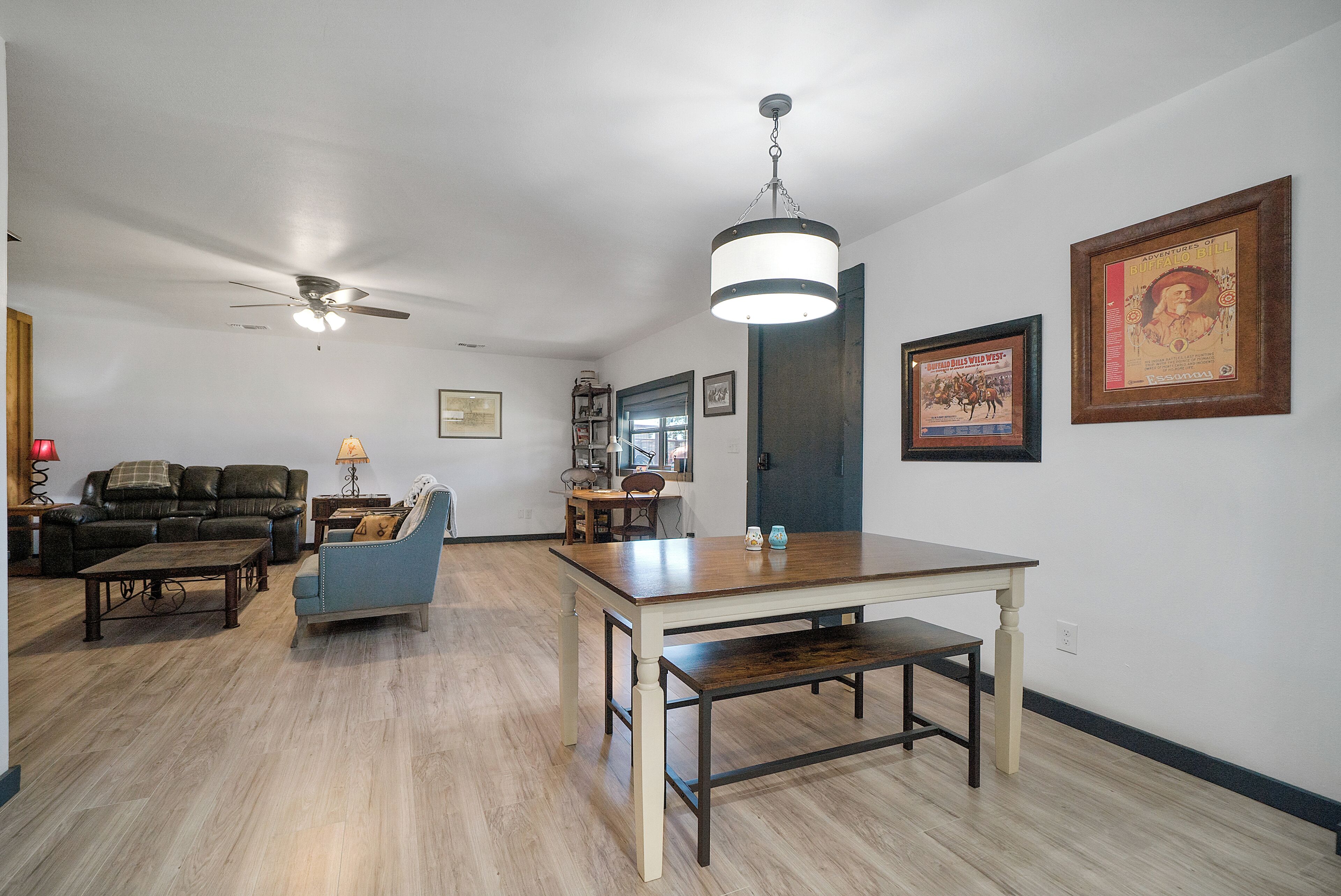A spacious living room with a wooden dining table, a blue armchair, a leather sofa, and a ceiling fan.