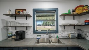 A kitchen with a large sink, coffee maker, toaster, and blender. There are shelves above the sink holding various items. - Faulkner Ranch Bunkhouse (Llano)