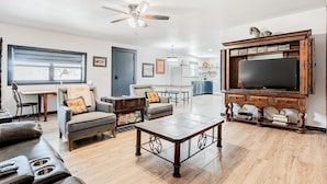 A spacious living room with a wooden coffee table, two sofas, a TV, and a ceiling fan. - Faulkner Ranch Bunkhouse (Llano)
