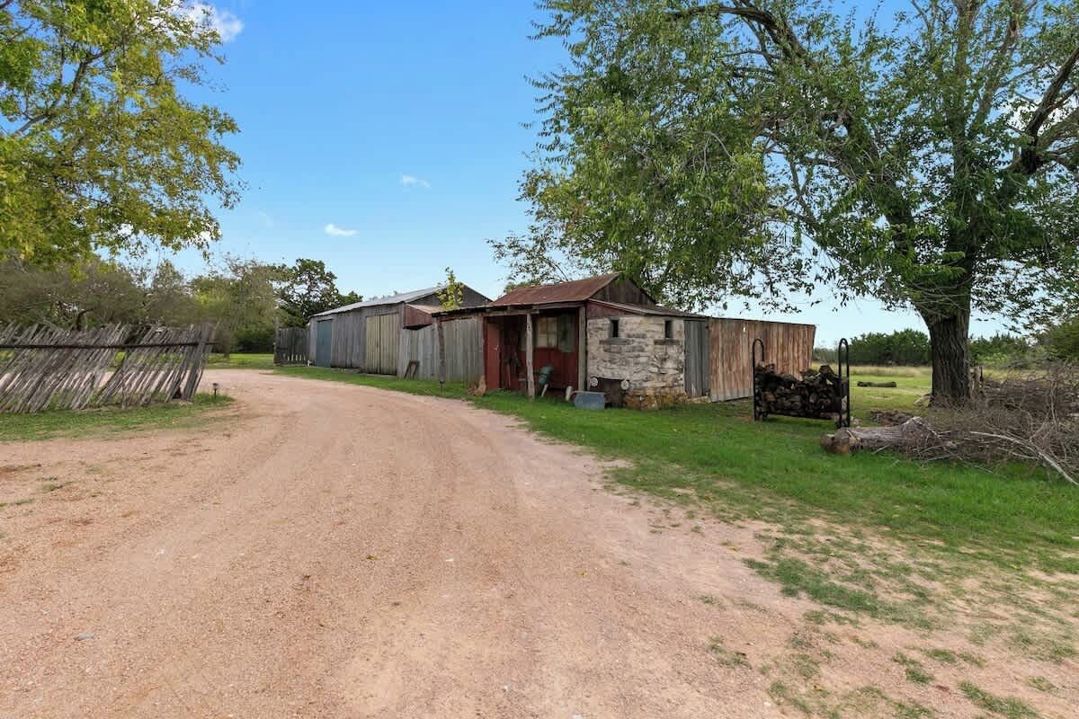 A rural road leading to a rustic barn with a wooden door and a stone wall.