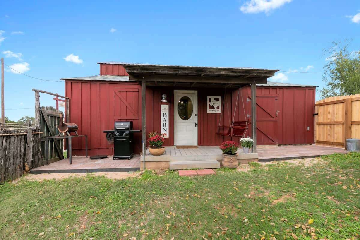 A red building with a white door, a small porch, and a wooden fence.