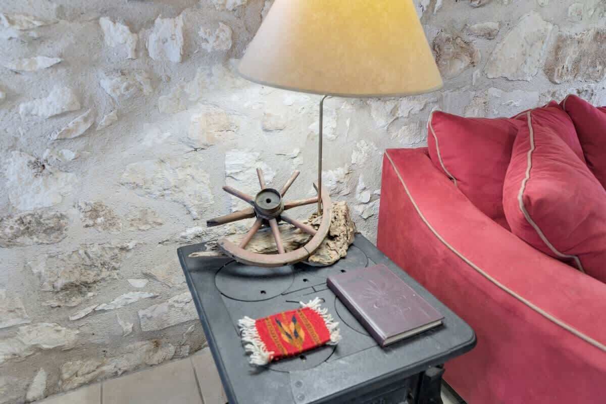 Un rincón acogedor con una lámpara de estilo vintage, un cojín rojo y una mesita con un libro y un objeto decorativo.