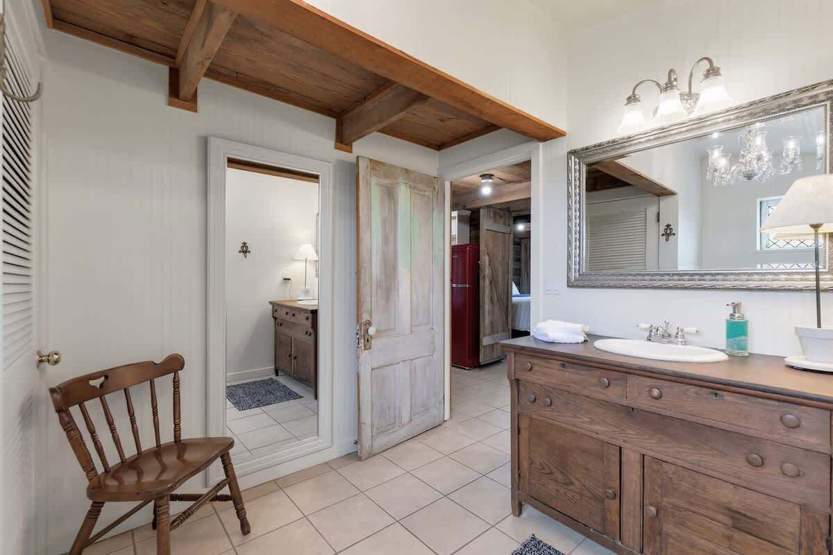 Een badkamer met een houten wastafel, een grote spiegel en een deur naar een andere kamer.