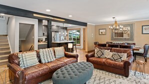 A spacious living room with leather sofas, a tufted ottoman, and a dining area with a chandelier. - Spacious & Chic! Ideal for Large Groups Near Resort with Private Hot Tub! (Steamboat Springs)