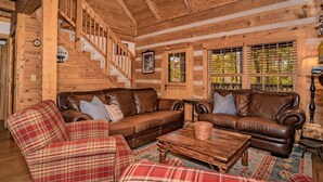 A log cabin interior with a wooden staircase, leather sofas, plaid furniture, and a wooden coffee table. - Rockin R Lodge (Sevierville)