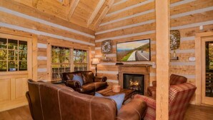 A log cabin interior with a fireplace, leather sofas, and a television mounted above it. - Rockin R Lodge (Sevierville)