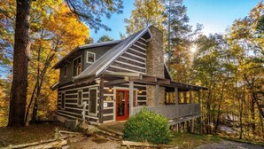 A log cabin with a red door, a stone chimney, and a porch. - Rockin R Lodge (Sevierville)