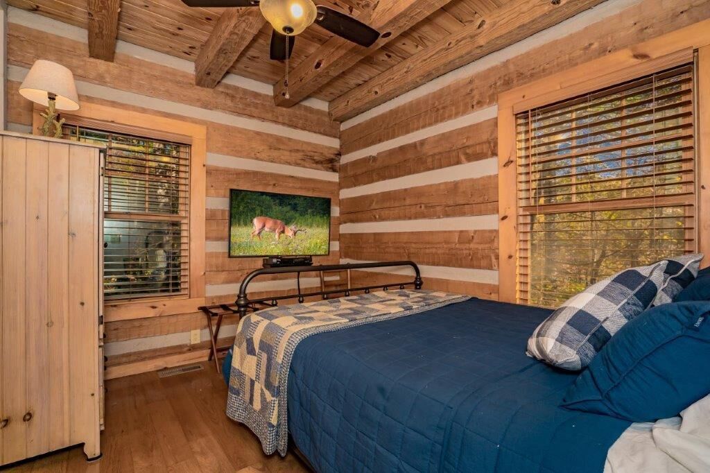 Un dormitorio tipo cabaña de madera con una cama, un televisor y una ventana con persianas.