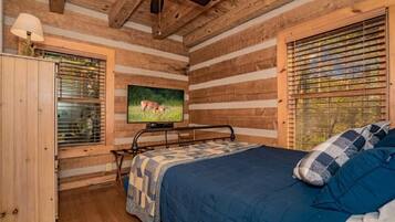 Un dormitorio tipo cabaña de madera con una cama, un televisor y una ventana con persianas.