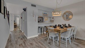 Une cuisine moderne avec une table à manger en bois, des chaises blanches et un luminaire suspendu.