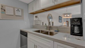 Une cuisine moderne avec des meubles blancs, un lave-vaisselle encastré, une machine à café et un miroir au-dessus de l’évier.