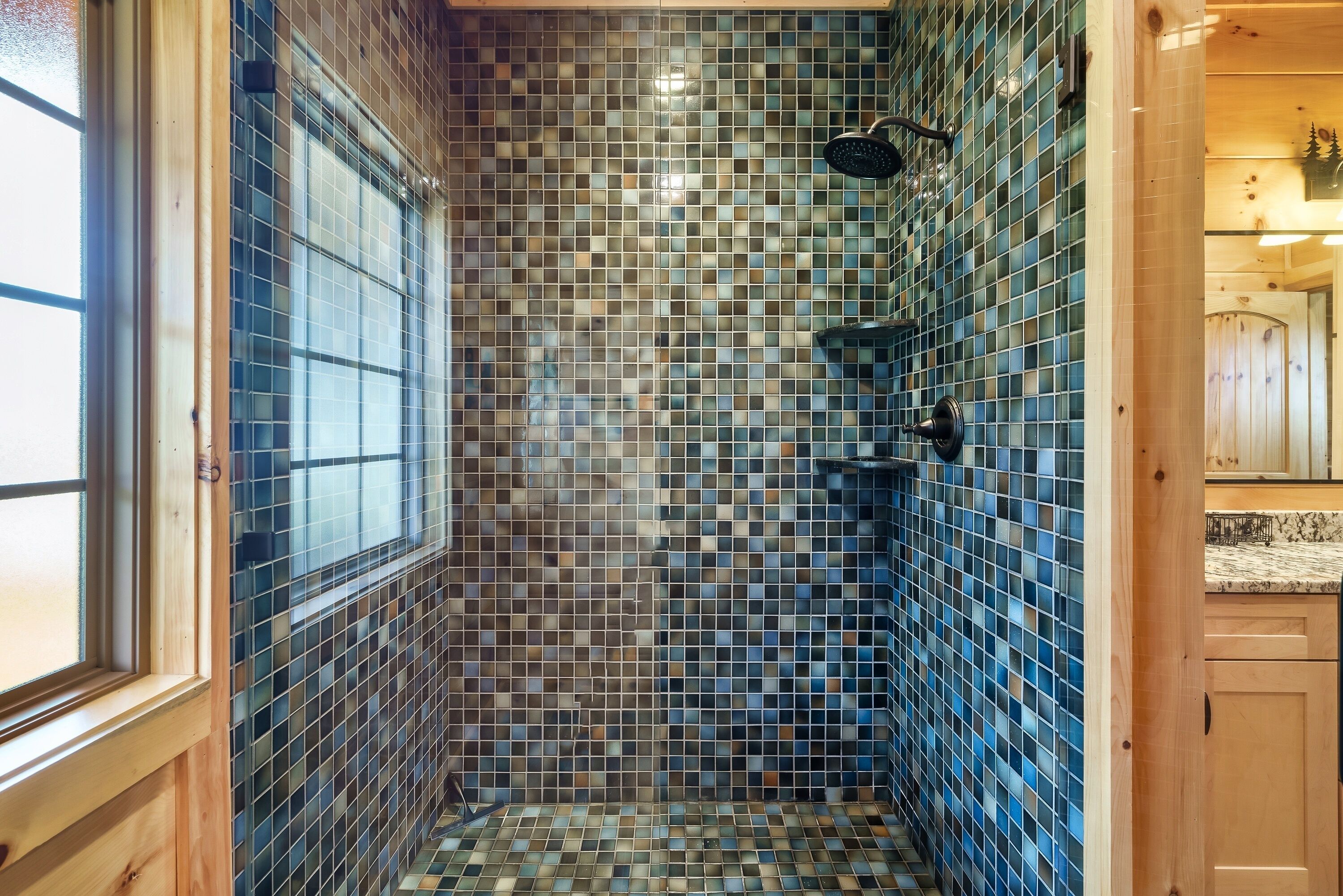 A shower with mosaic tiles, wooden walls, and a visible window.
