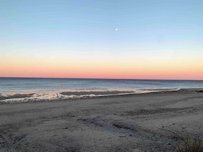 A beach with a clear sky and a visible moon.