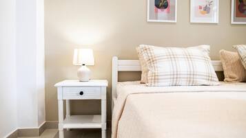 Un dormitorio ordenado con cama, una mesita de noche con lámpara y una pared decorada con cuadros.