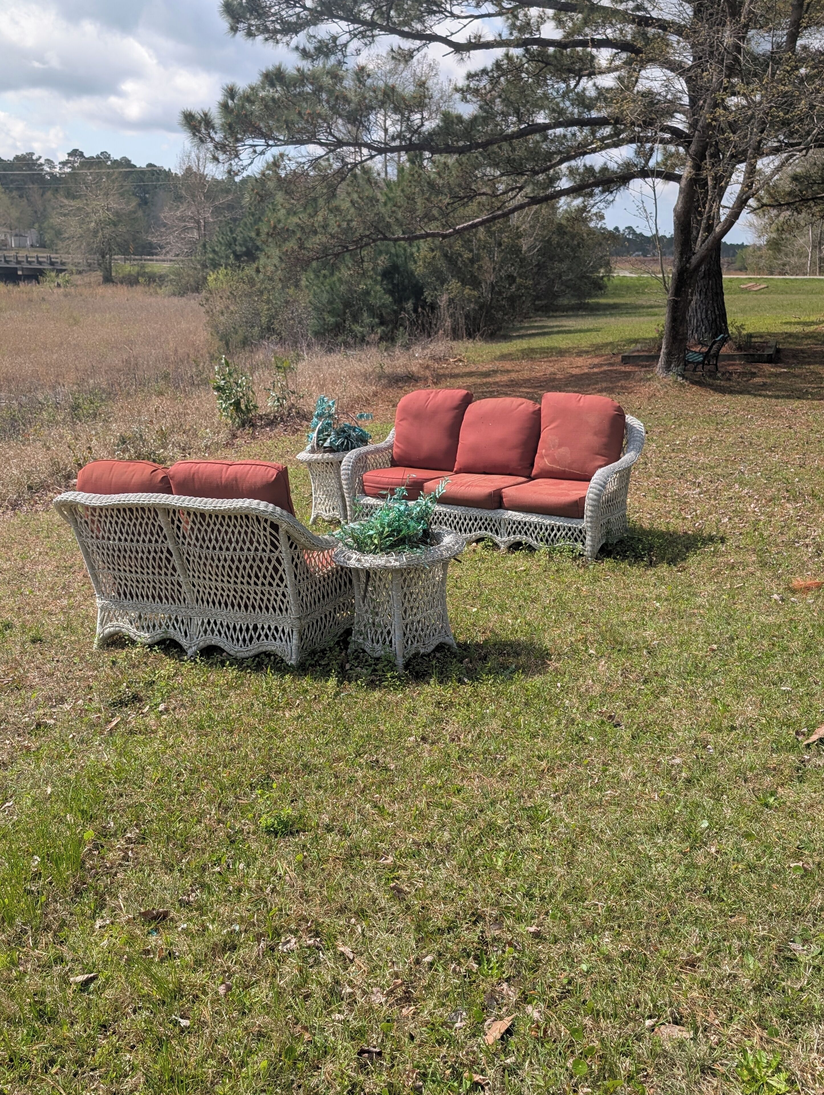 Un espace de détente extérieur aménagé avec des meubles en osier et des coussins rouges, entouré de pelouse et d’arbres.